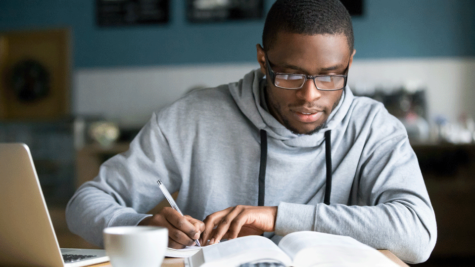 Ein Mann mit Brille schreibt in ein Heft (Source: iStock - fizkes) Ein Mann mit Brille schreibt in ein Heft
